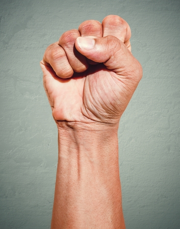 Riot protest fist raised in the air. Male clenched fist on dark grunge background.の写真素材
