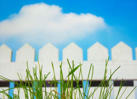 White picket fence and sky with green grassの写真素材