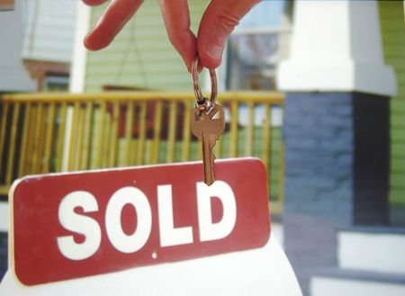 Hand holding a house key in front of a  sold signの写真素材