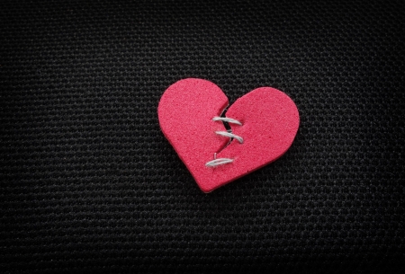 broken red heart with threaded stitches, on dark background                               の写真素材