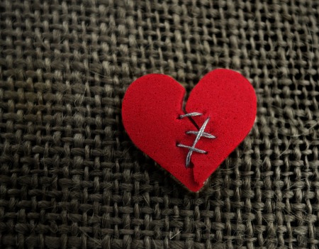 Red broken heart stitched with thread on textured backgroundの写真素材