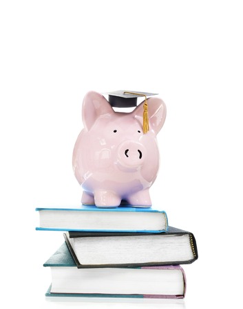 pink piggy bank with graduation cap on stack of booksの写真素材