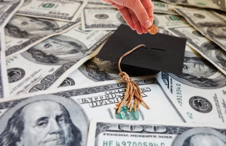 Hand putting money into a graduation cap -- student loan repayment or college savings concept