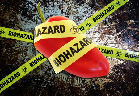 Yellow biohazard tape across a pepper -- food safety conceptの写真素材