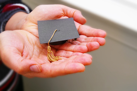Woman holding a miniature graduation cap in her handsの写真素材