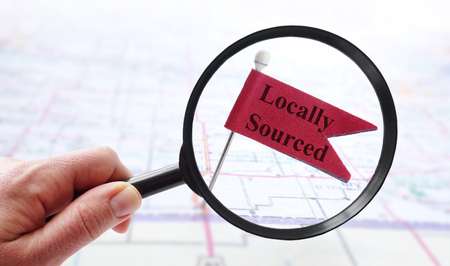 Hand holding a magnifying glass over Locally Sourced pin flagの写真素材