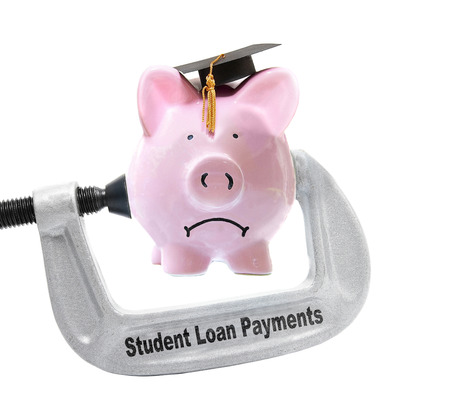 Frowning piggy bank wearing graduation cap being squeezed in a Student Loan Payments vice, on white -の写真素材