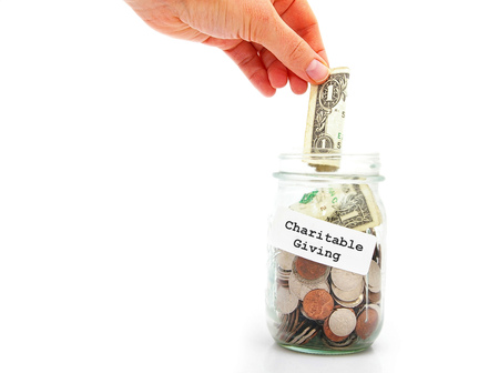 hand putting a dollar into Charitable Giving jar, isolated on whiteの写真素材