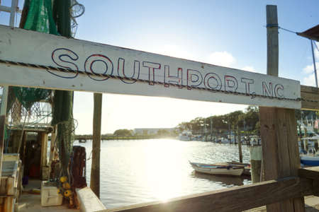 A weathered Southport , NC sign hangs at a dock in front of a fishing boat on the Cape Fear Riverの写真素材