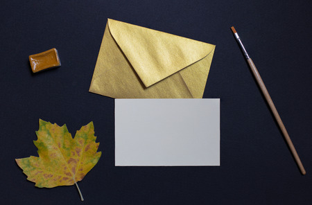 Autumn leaf on black background with card invitation and golden envelopeの写真素材