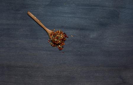 Wooden spoon with condiment (pepper, garlic, basil) on dark background. Top view