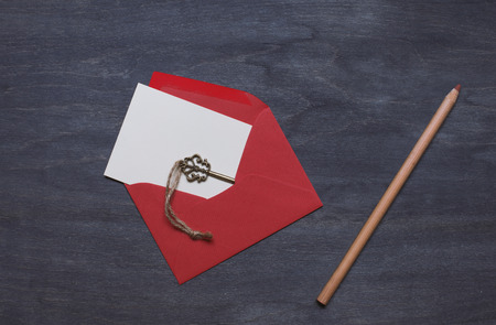 Open red envelope on dark wood background with key and pencilの写真素材