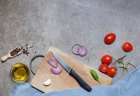 Tomatoes, onion and olive oil on grey stone background with cutting board. Top viewの写真素材