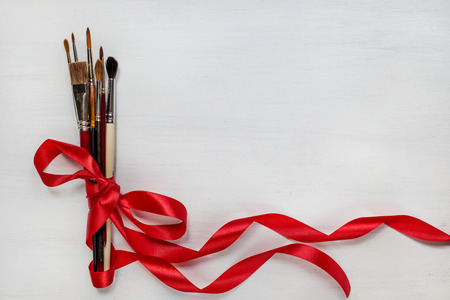 Different watercolor paintbrushes with red ribbon on white wooden background. Top view.の写真素材