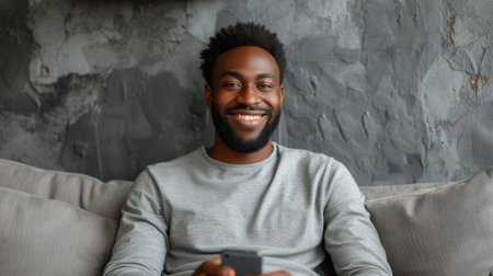 The image features a smiling African American man as he uses a mobile phone with a new application while seated in an armchair over a gray wall. The background has a panorama and there is an emptyの素材