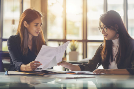 An office worker with a disability and her female colleague working together on paperwork.の素材