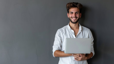 Businessman wearing a light shirt posing isolated on a gray wall background in a studio portrait. Achievement career wealth business concept mock up. Holding a laptop desktop computer..の素材