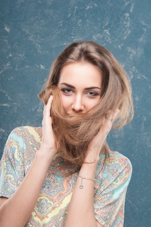 Emotional cheerful young dark-blonde woman with long hair standing in half length on creative backgroundの写真素材