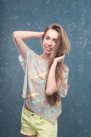 Emotional cheerful young dark-blonde woman with long hair standing in half length on creative backgroundの写真素材