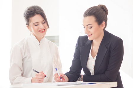 Two  attractive friendly young businesswomen talking and smiling to each other at informal meeting in modern officeの写真素材