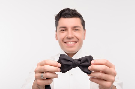 Young caucasian dark hair man smiling takes his bow tie in handsの写真素材