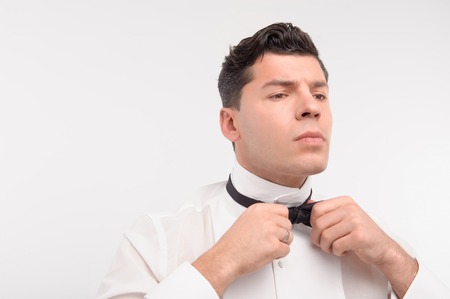 Cool young Caucasian dark hair man tie up his bow isolated on whiteの写真素材