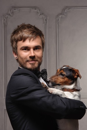 Young man is holding his sweet puppy isolated on old room backgroundの写真素材