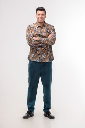 Front view of full length portrait of handsome young man in colored shirt looking at camera isolated on whiteの写真素材