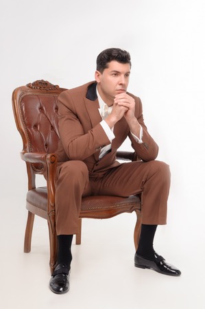 Young attractive serious man in brown suit sitting in armchair isolated on white backgroundの写真素材