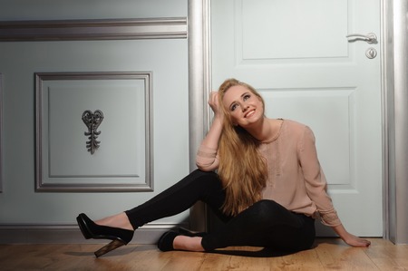 Young attractive smiling woman sitting and dreaming on classic interior blue backgroundの写真素材