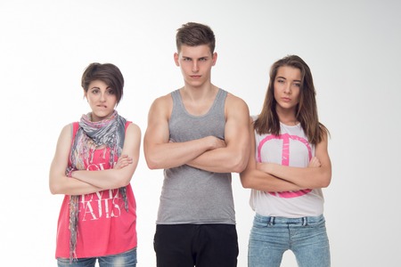 Waist-up portrait of two attractive teen girls and a boy looking angry, mistrustfully, with contempt. Isolated on white background.の写真素材