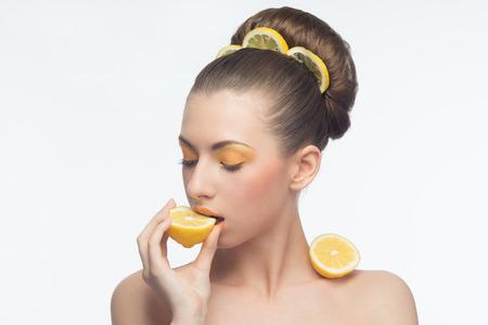Beautiful young woman with oranges in her hands and hair, orange makeup isolated on white backgroundの写真素材