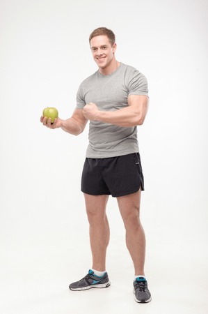 Full length portrait of an athletic man holding a fresh apple and showing muscles, isolated over a white background  Concept of sport, healthの写真素材