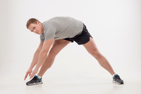 Full length portrait of young smiling man athlete doing warming exercises isolated on white...