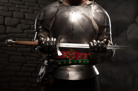 Closeup portrait of medieval knight in armor holding a sword in dark stone wall backgroundの写真素材
