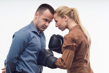 Young attractive business woman in boxing gloves attacking man with fists, isolated on white backgroundの写真素材