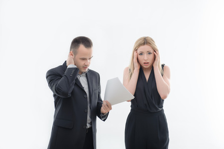 Angry boss businessman with blank paper and embarrassed young attractive woman employee holding her head and looking at camera, isolated on whiteの写真素材