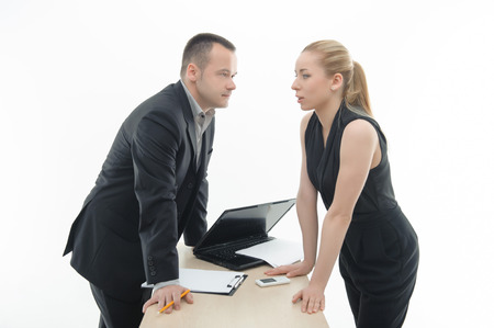 Waistup portrait of young attractive colleagues discussing something, arguing by the table with laptop and clipboard, isolated on whiteの写真素材