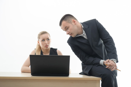 Two business people discussing a problem, man in elegant suit sitting on desk with pencil, attractive blonde woman at laptop isolated on whiteの写真素材