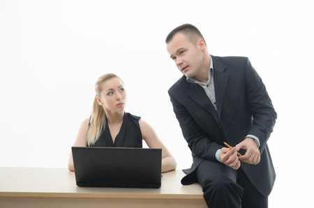 Two business people discussing a problem, man in elegant suit sitting on desk with pencil, attractive blonde woman at laptop isolated on whiteの写真素材