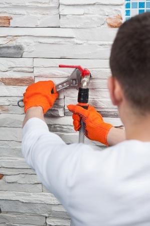 Plumber in orange gloves  mounting a flexible pipe to a valve with adjustable spanner monkey wrench...