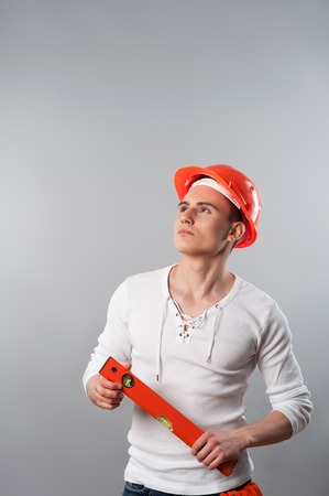 Portrait of a young serious handsome worker in helmet holding spirit level looking up isolated on grey backgroundの写真素材