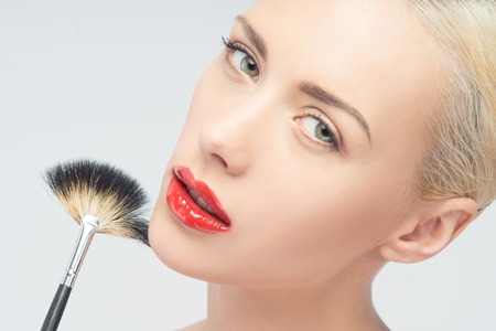 Portrait of beautiful young blonde woman applying makeup with brush, Isolated on White Backgroundの写真素材