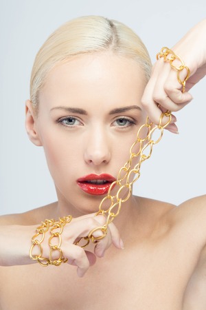 Portrait of young sexy blonde woman holding golden chain isolated on whiteの写真素材