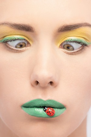 Closeup portrait of beautiful woman with yellow green makeup kidding and squinting on her lips with decorative ladybirdの写真素材
