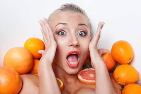 Sexual young blonde seductive woman posing in the bathtub with oranges, holding her head in surprise, closeup portraitの写真素材