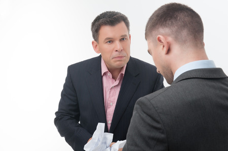 Senior and junior business people in elegant suits  Boss angry with young handsome employee standing from behind, holding crumpled paper isolated on whiteの写真素材