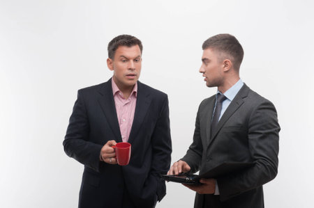 Senior and junior business people discuss something during their meeting holding coffee cup and tablet, isolated on white backgroundの写真素材