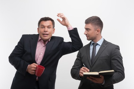 Senior and junior business people discuss something, boss holding coffee cup leans on shoulder of young employee, isolated on white backgroundの写真素材