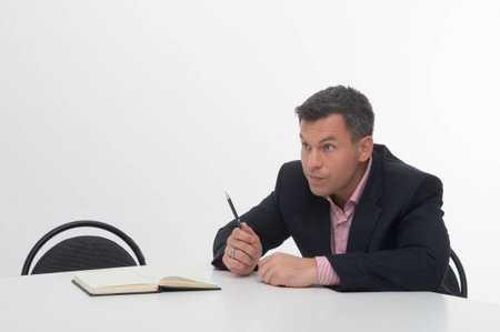 Senior mature manager sitting at desk, pointing with pen aside, isolated on whiteの写真素材